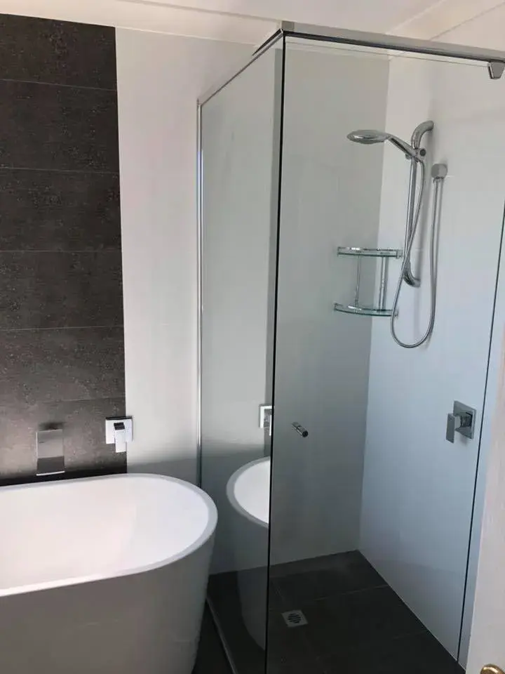 Dark feature wall tiling beside a freestanding bath and frameless shower