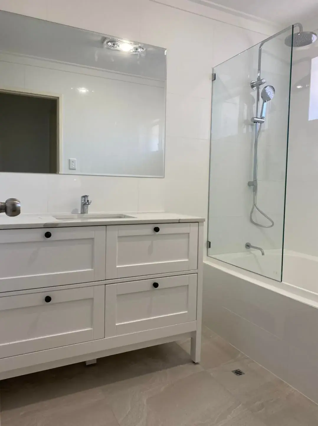 White floor-to-ceiling wall tiling in a renovated bathroom with shaker vanity